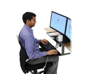 Ergotron WorkFit-S Dual, Black Colour, Side View, Lowered Workstation, Office Usage, Person Typing, Man Sitting, Keyboard, Mouse, Two Monitors